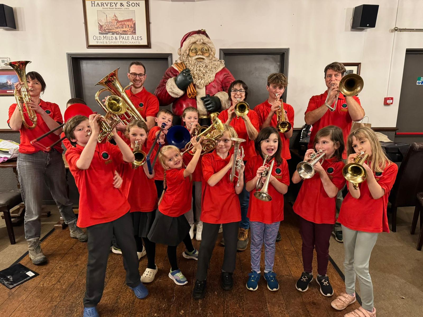 Child and adult brass players pose in front of a Santa Claus figure