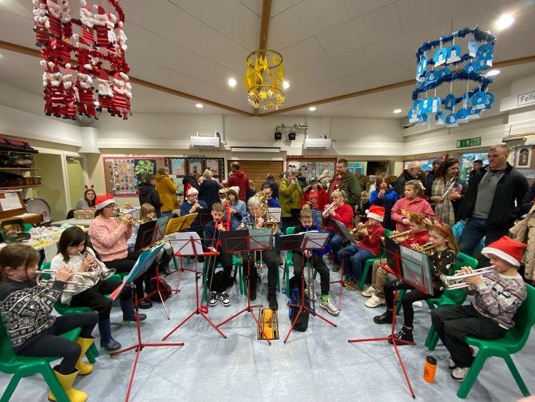 Adults and children playing brass instruments at an indoor Christmas event.